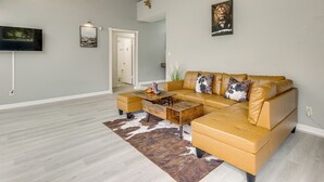 A spacious living room with a large L-shaped leather sofa, a wooden coffee table, and a mounted flat-screen TV. - Quick Hwy Access: Family Retreat in Houston (Houston)