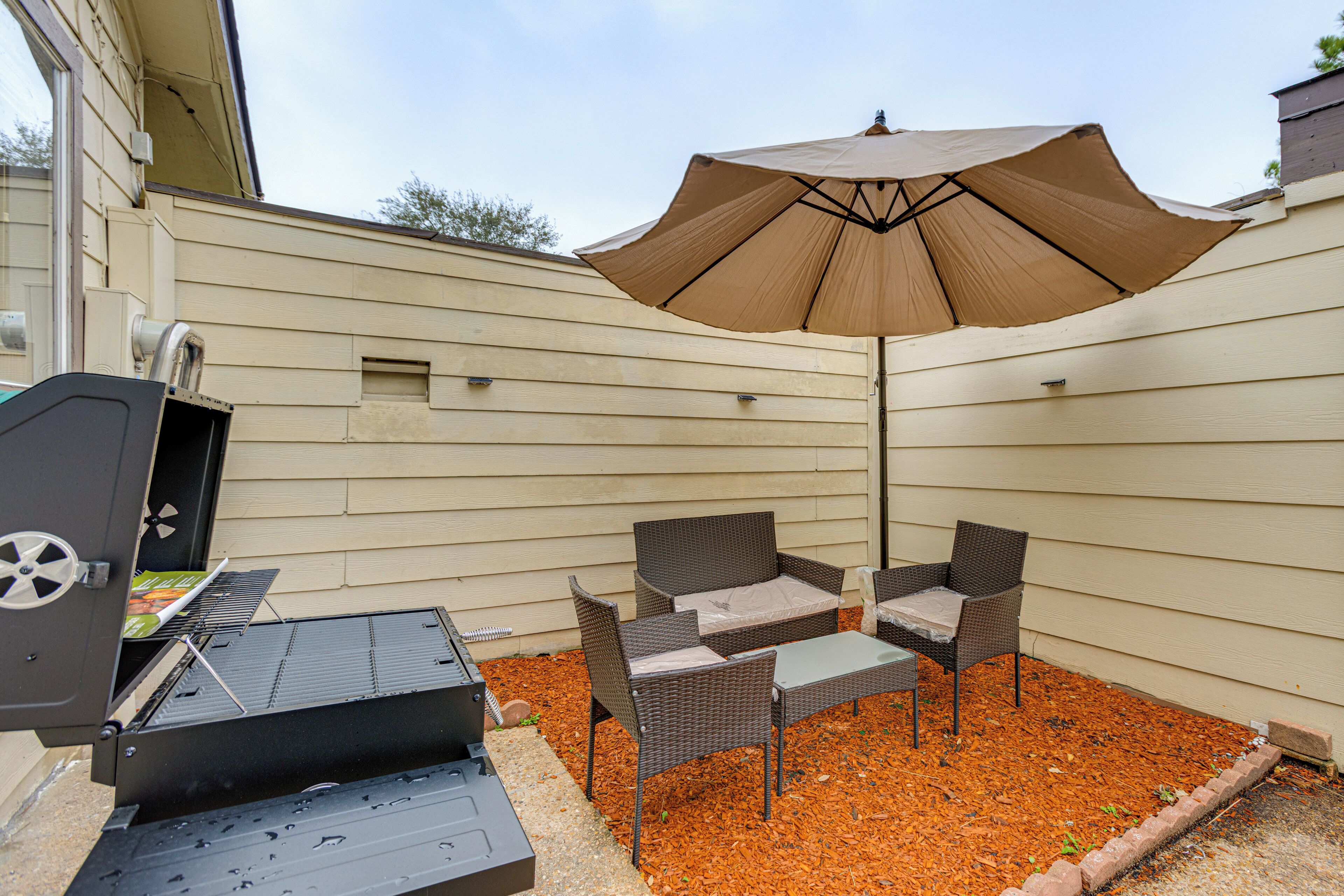 A backyard with a grill, wicker furniture, and an umbrella.
