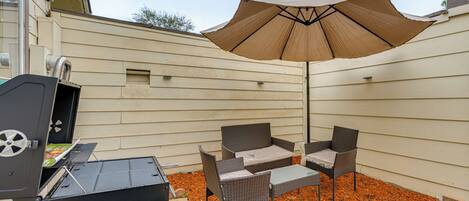 A backyard with a grill, wicker furniture, and an umbrella.