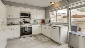 A kitchen with white cabinets, a microwave, stove, and a dishwasher. There is a window with blinds and a view of the outside. - Quick Hwy Access: Family Retreat in Houston (Houston)