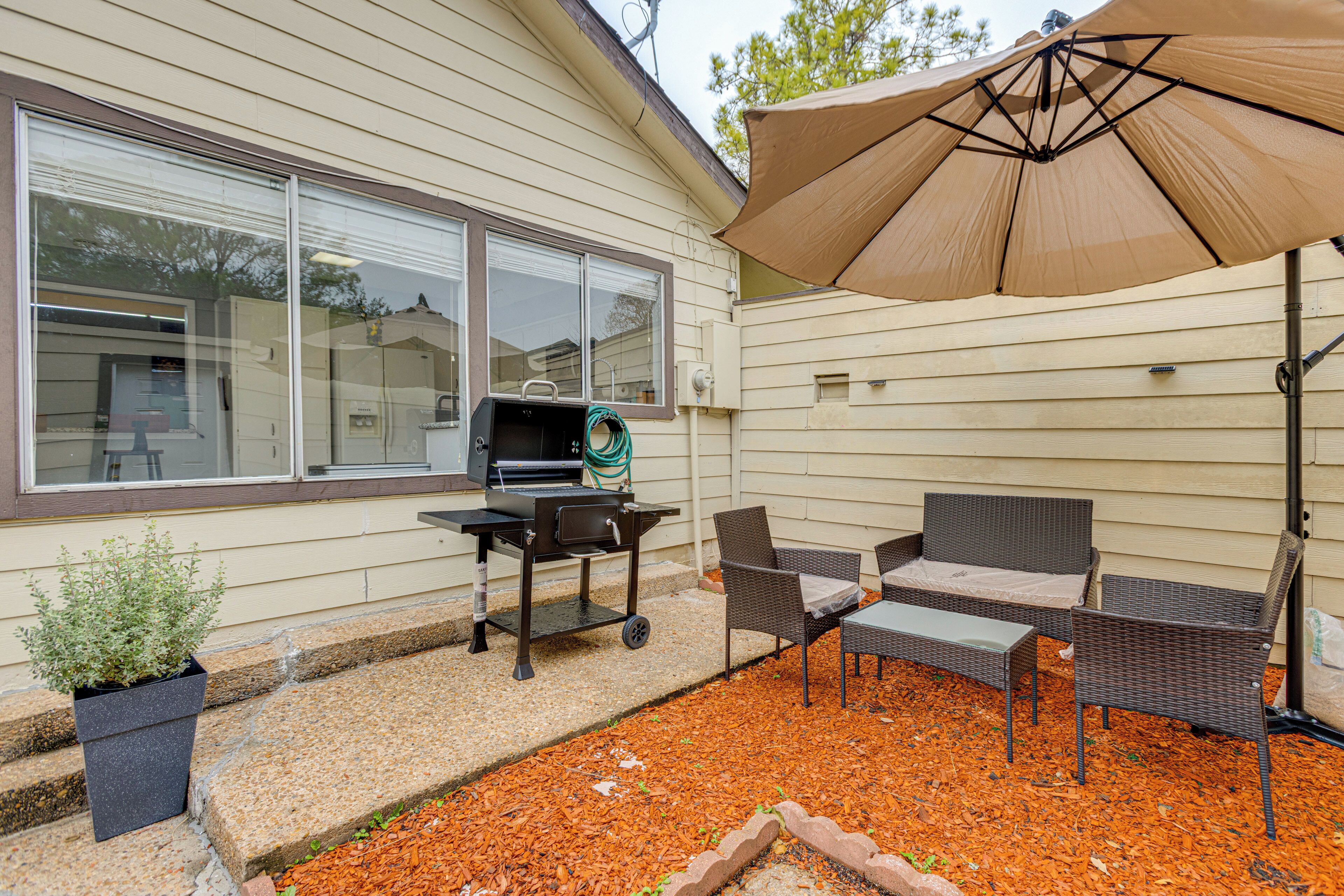 Un patio con mobiliario exterior, una parrilla y un gran paraguas.