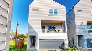Ein zweistöckiges Haus mit Garage, Balkon mit Sitzgelegenheiten und einem kleinen, umzäunten Garten.