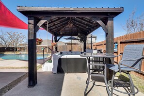 A covered outdoor patio with a hot tub, seating area, and a wooden fence in the background. - Pool & Hot Tub! Dog-friendly Awaysis in SE Austin (Del Valle)