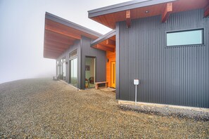 Un bâtiment moderne avec une allée en gravier, un avant-toit en bois et une grande fenêtre.