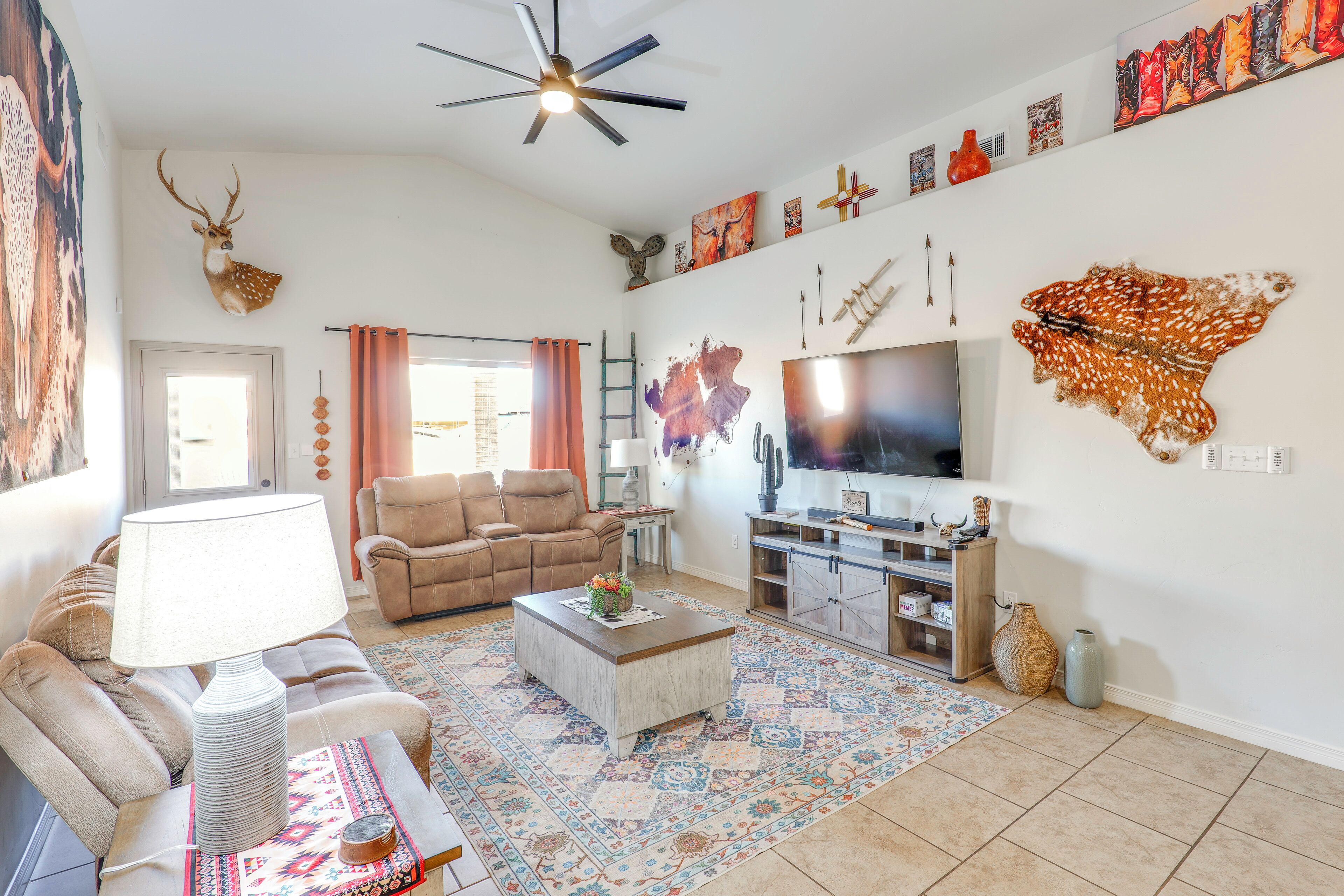 A living room with a sofa, coffee table, and a TV. There are wall decorations and a ceiling fan.