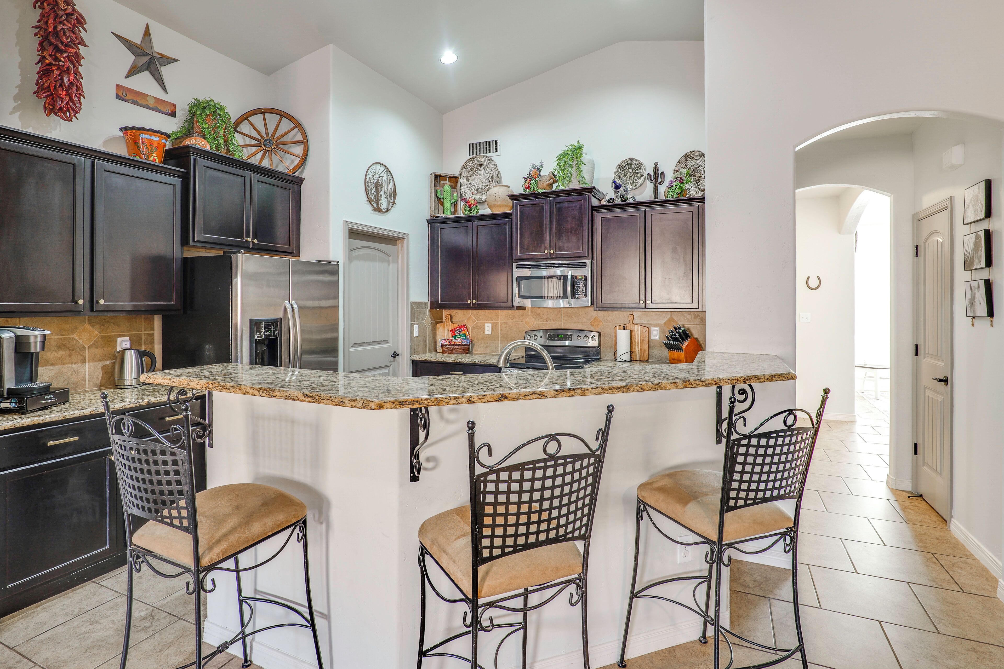 A kitchen with dark cabinets, a stainless steel refrigerator, a microwave, and a large island with bar stools.
