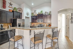 A kitchen with dark cabinets, a stainless steel refrigerator, a microwave, and a large island with bar stools. - Fire Pit, Pets Welcome: Home 4 Mi to Dtwn Carlsbad (Carlsbad)