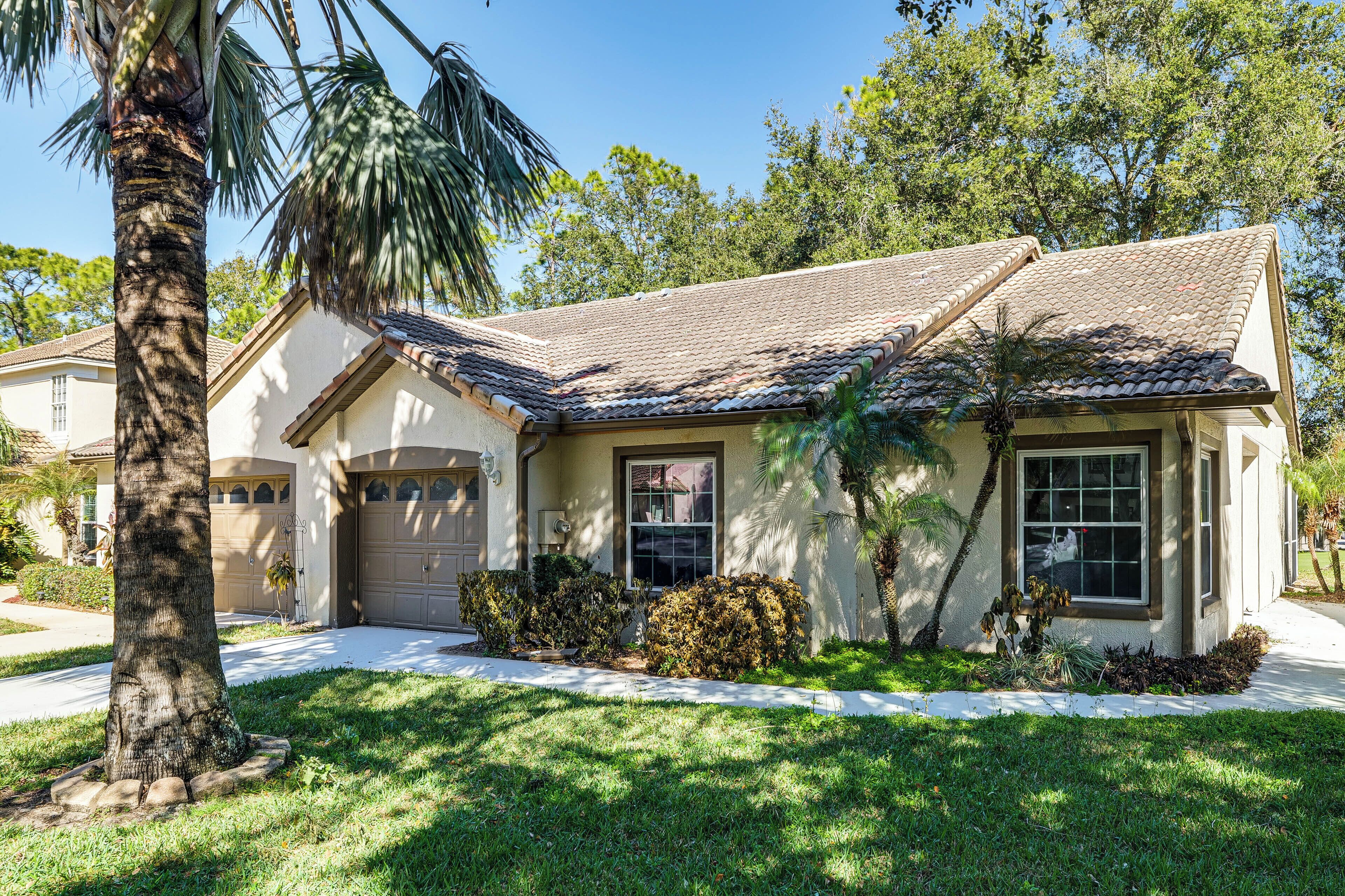 A single-story house with a tiled roof, a garage, and a well-maintained lawn with a palm tree.
