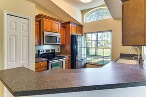 Una cocina con armarios de madera, un refrigerador de acero inoxidable, un microondas y un amplio ventanal con vistas al exterior.