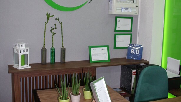 Una mesa de recepción con un cartel que dice 'grupo principal', una pantalla digital, certificados enmarcados y plantas en macetas.