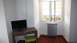 Una habitación pequeña con escritorio, silla, radiador y ventana que da a plantas en macetas afuera.