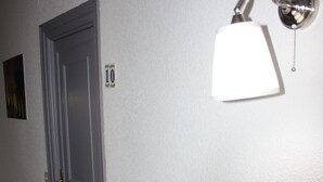 Un pasillo con una puerta blanca marcada con el número 10, una lámpara de pared y un pequeño cuadro en la pared.