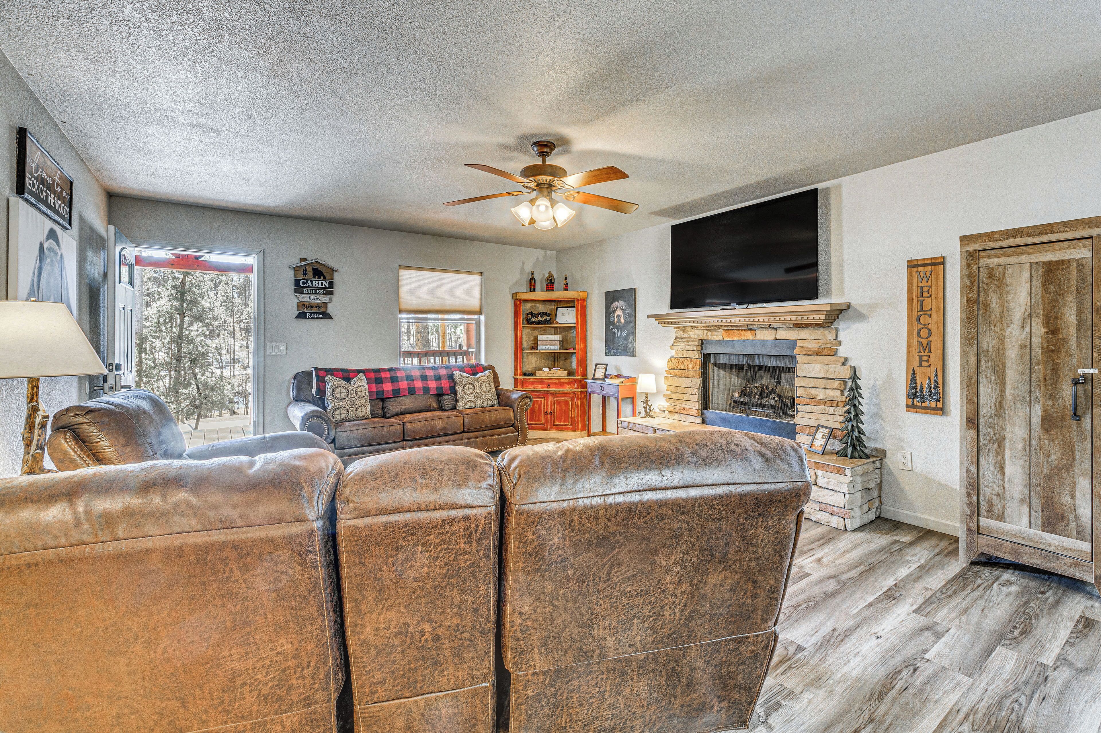 A living room with leather sofas, a fireplace, a television, and a ceiling fan.