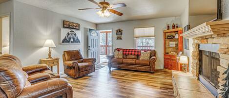 A spacious living room with leather sofas, a fireplace, and a ceiling fan.