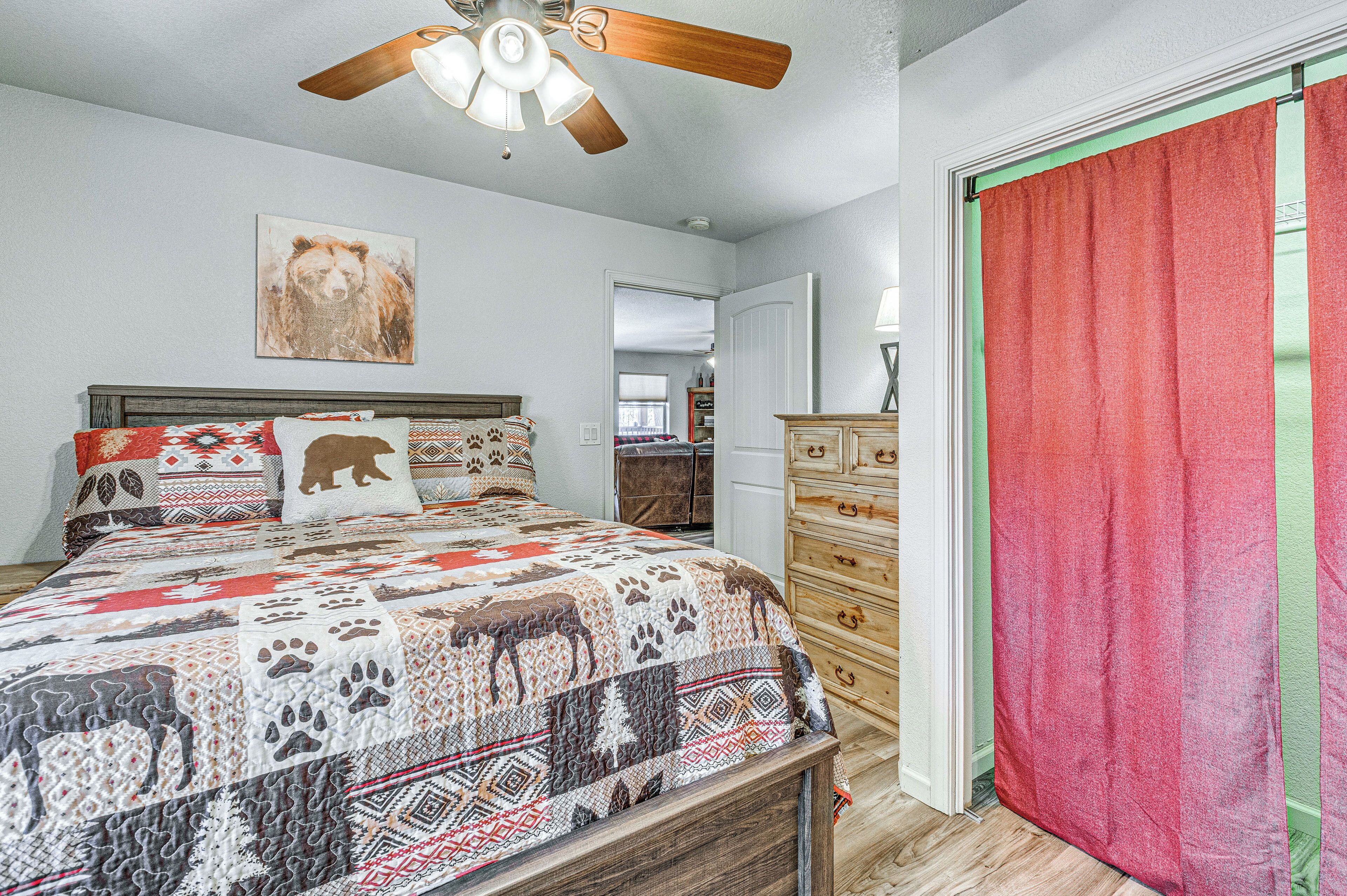 A bedroom with a bed, a ceiling fan, a wooden dresser, and a red curtain.