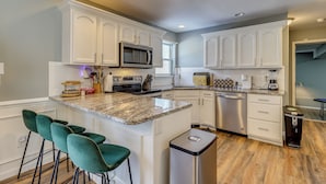 A modern kitchen with white cabinets, a granite countertop, and a stainless steel dishwasher. There are three bar stools and a trash can. - Family Retreat w/ Game Room, 4 Mi to Kalahari! (Long Pond)