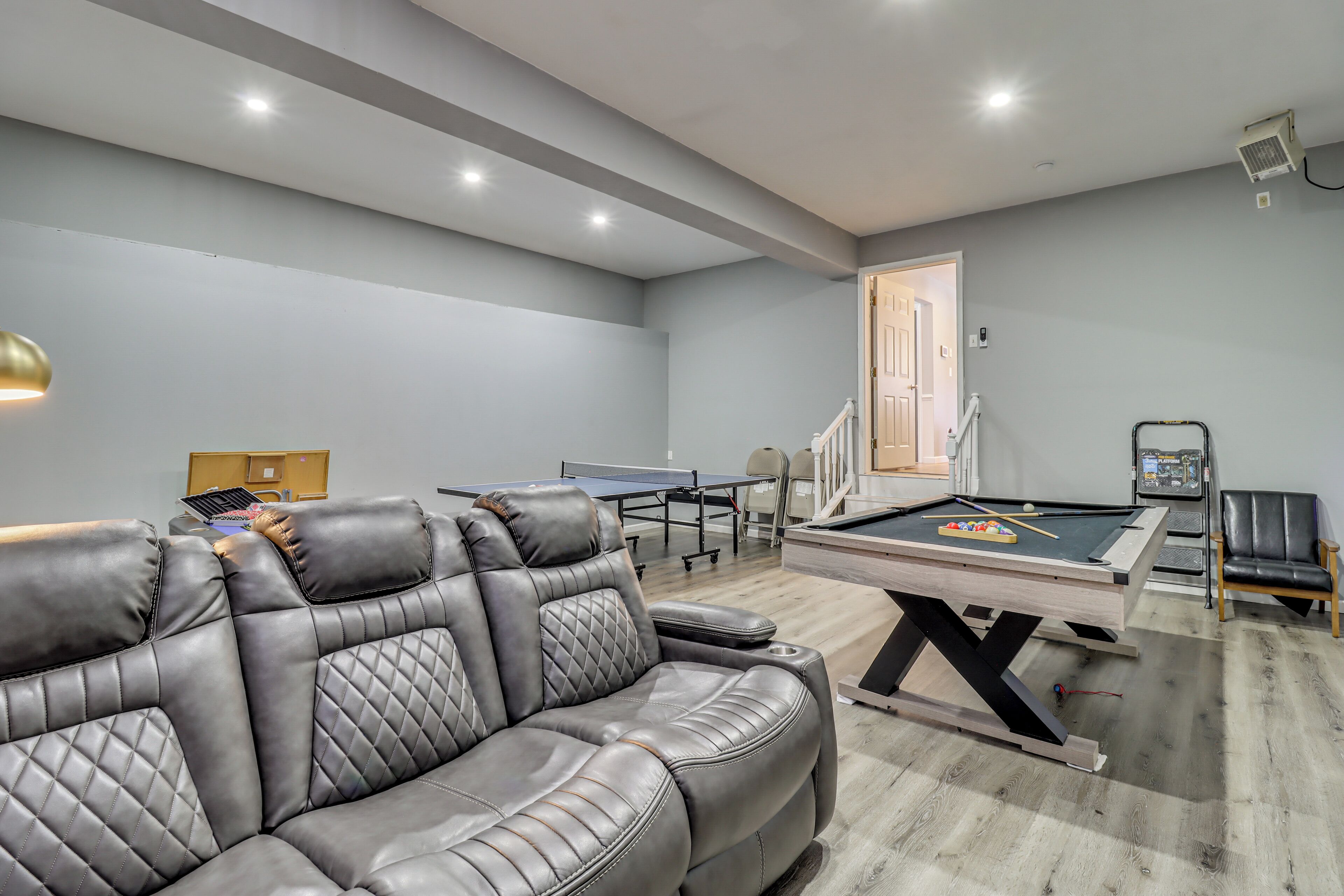 A modern living room with a pool table, leather sofa, and a ping pong table.
