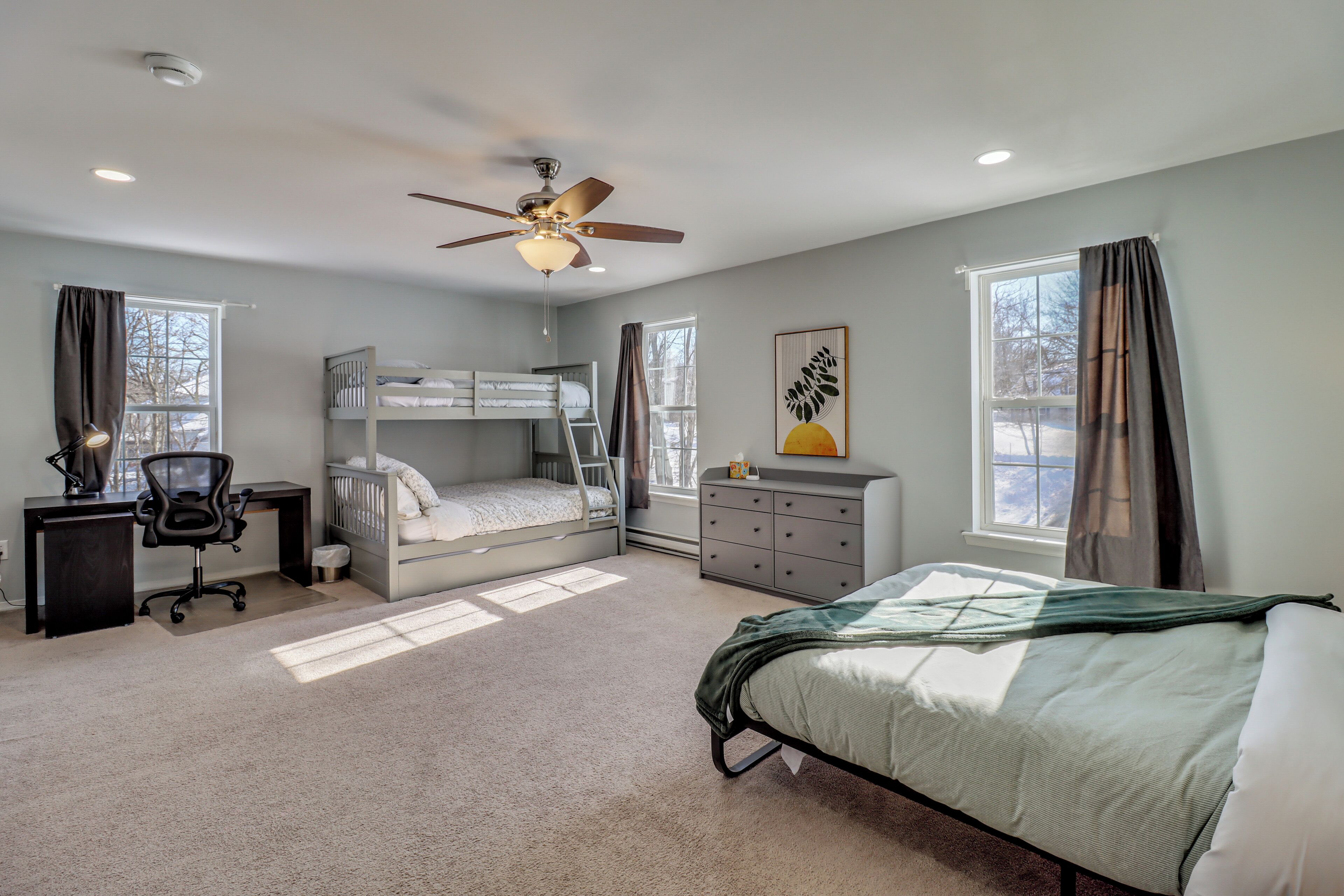 A bedroom with bunk beds, a desk, a chair, a dresser, and a ceiling fan.