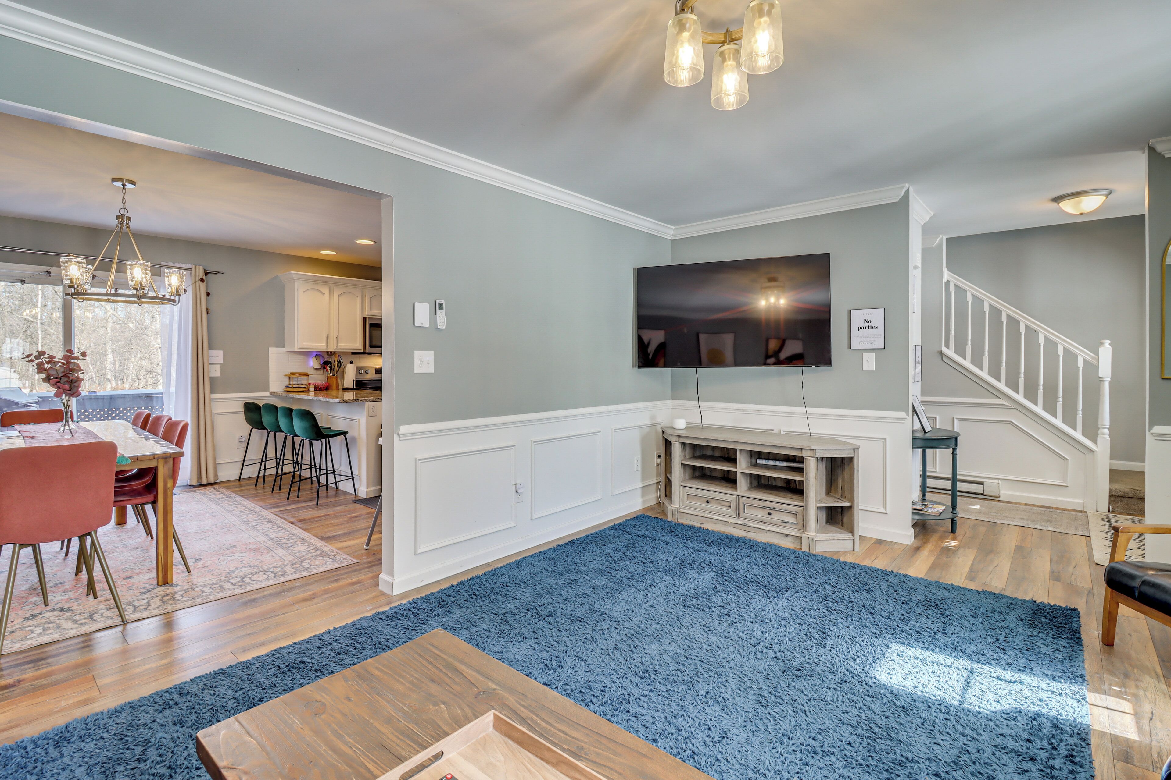 A spacious living room with a blue carpet, wooden coffee table, and a TV mounted on the wall.