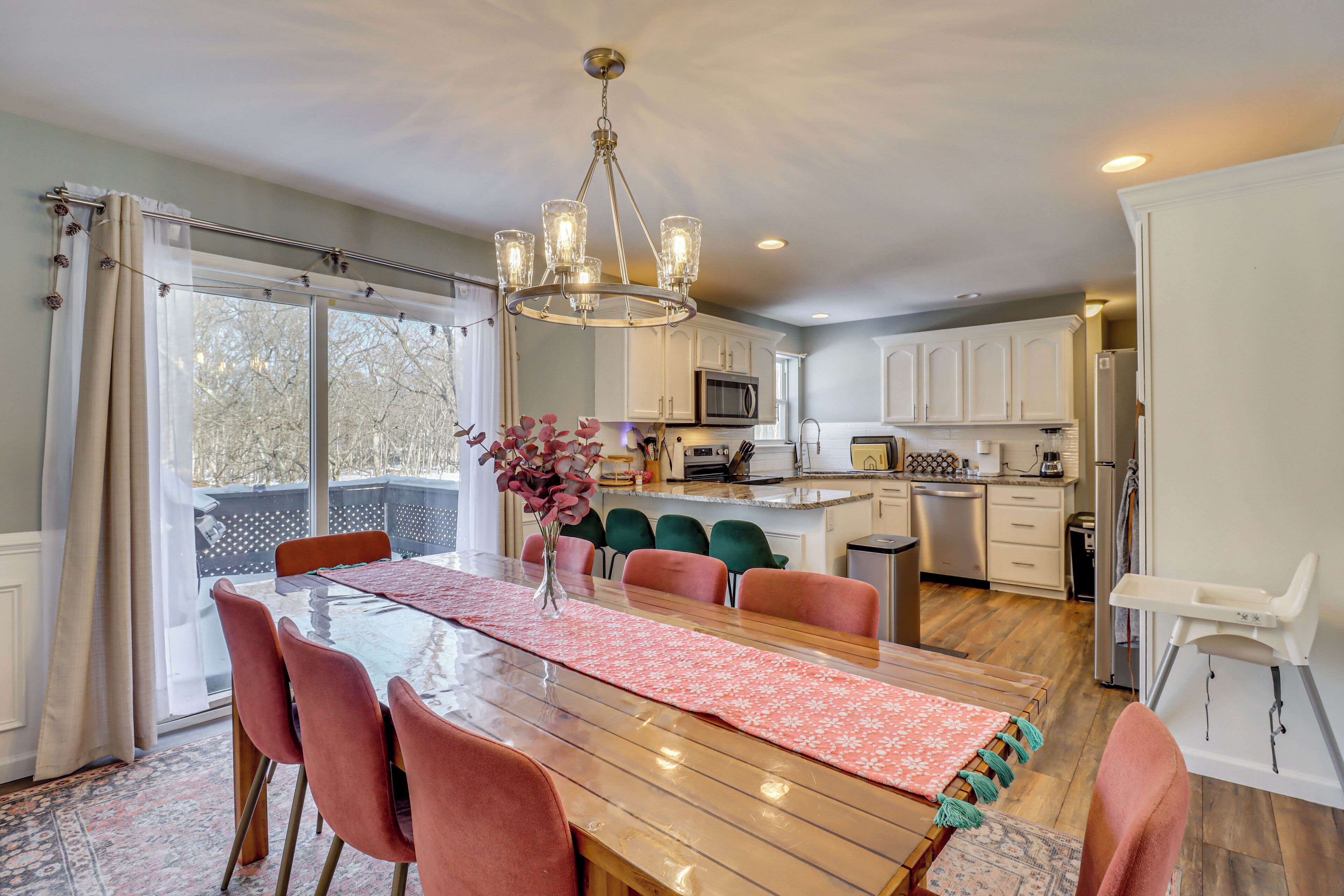 A spacious dining area with a wooden table, pink chairs, and a chandelier.