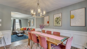 A dining area with a wooden table, pink chairs, and a chandelier. There are framed artworks on the walls and a blue rug on the floor. - Family Retreat w/ Game Room, 4 Mi to Kalahari! (Long Pond)