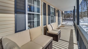 A covered porch with beige sofas and wicker furniture, a snow-covered landscape in the background, and a wooden railing. - Family Retreat w/ Game Room, 4 Mi to Kalahari! (Long Pond)