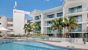 Un hôtel moderne doté d’une piscine, de palmiers et surplombant un ciel d’un bleu limpide.