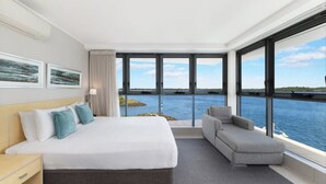 Une chambre d’hôtel moderne, dotée d’un grand lit, d’un canapé et offrant une vue sur la mer grâce à de grandes fenêtres.