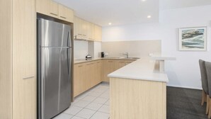 Une cuisine moderne avec des meubles en bois clair, un réfrigérateur en acier inoxydable et un plan de travail blanc.