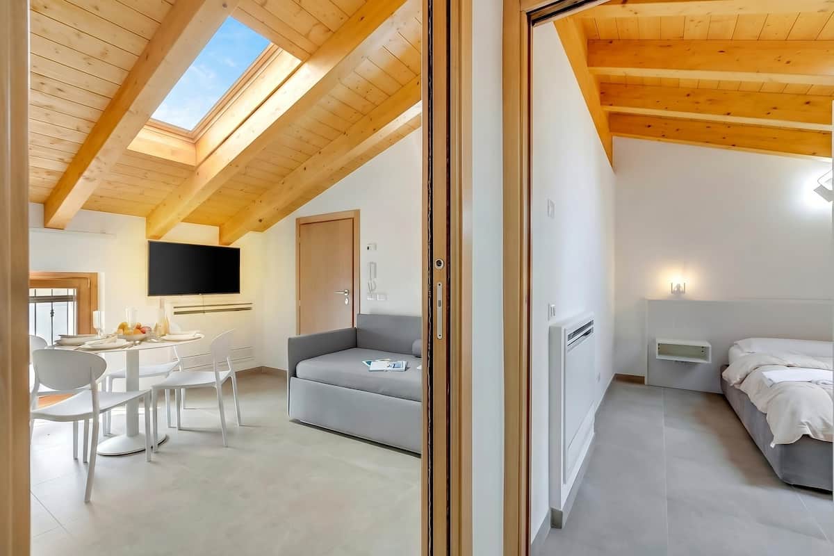 A modern room with a wooden ceiling, a flat-screen TV, a sofa, a bed, and a dining area with chairs and a table.