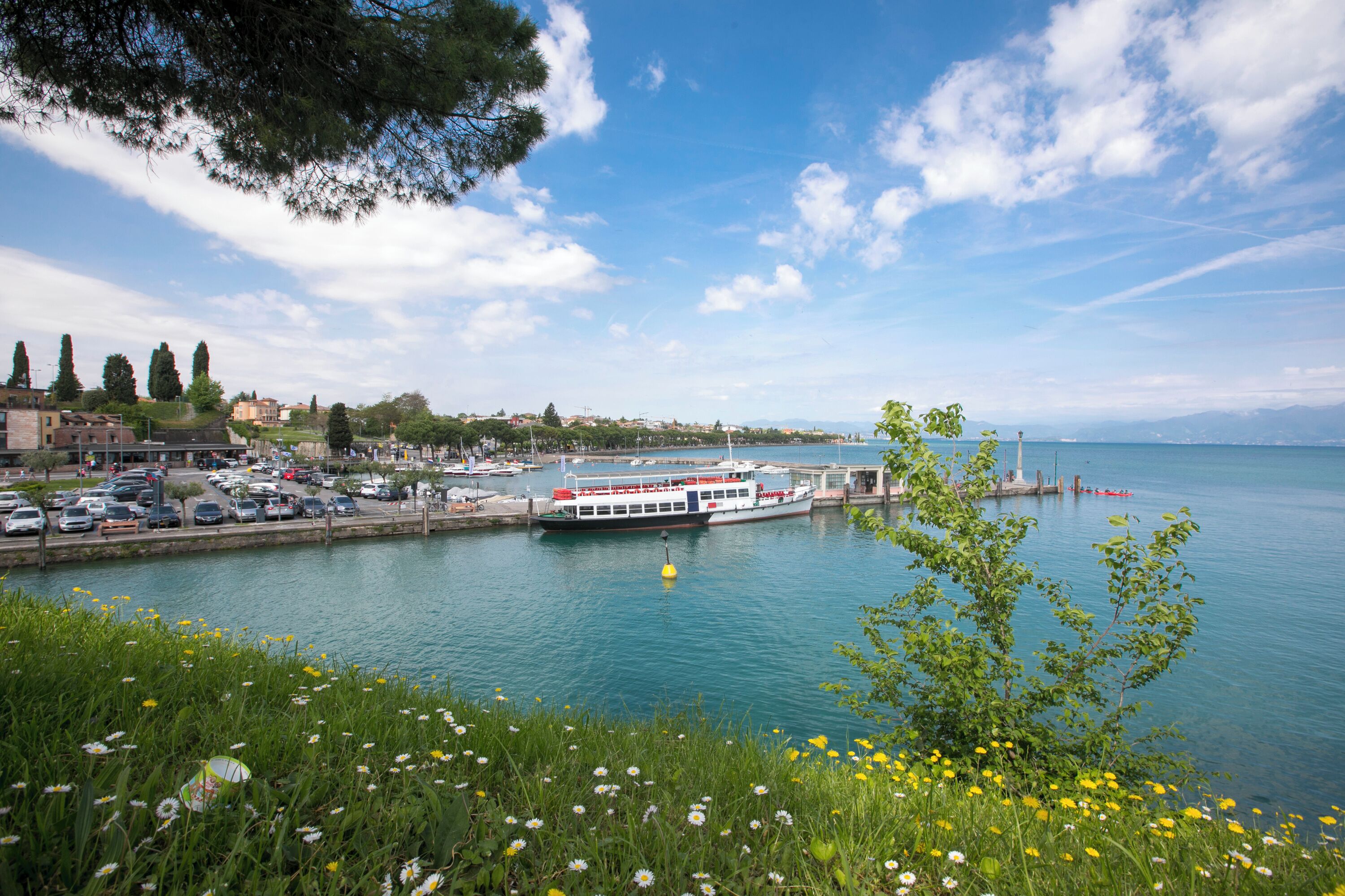 A waterfront view with a boat docked at a pier, a marina with boats, and a cityscape in the background.