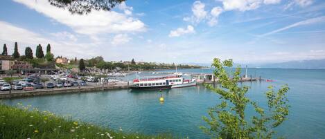 A waterfront view with a boat docked at a pier, a marina with boats, and a cityscape in the background.