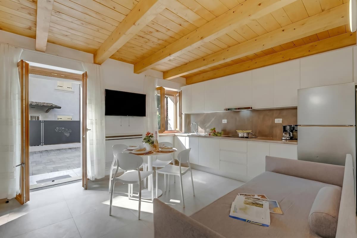 A modern kitchen with white cabinets, a flat-screen TV, and a dining area with white chairs and a table.