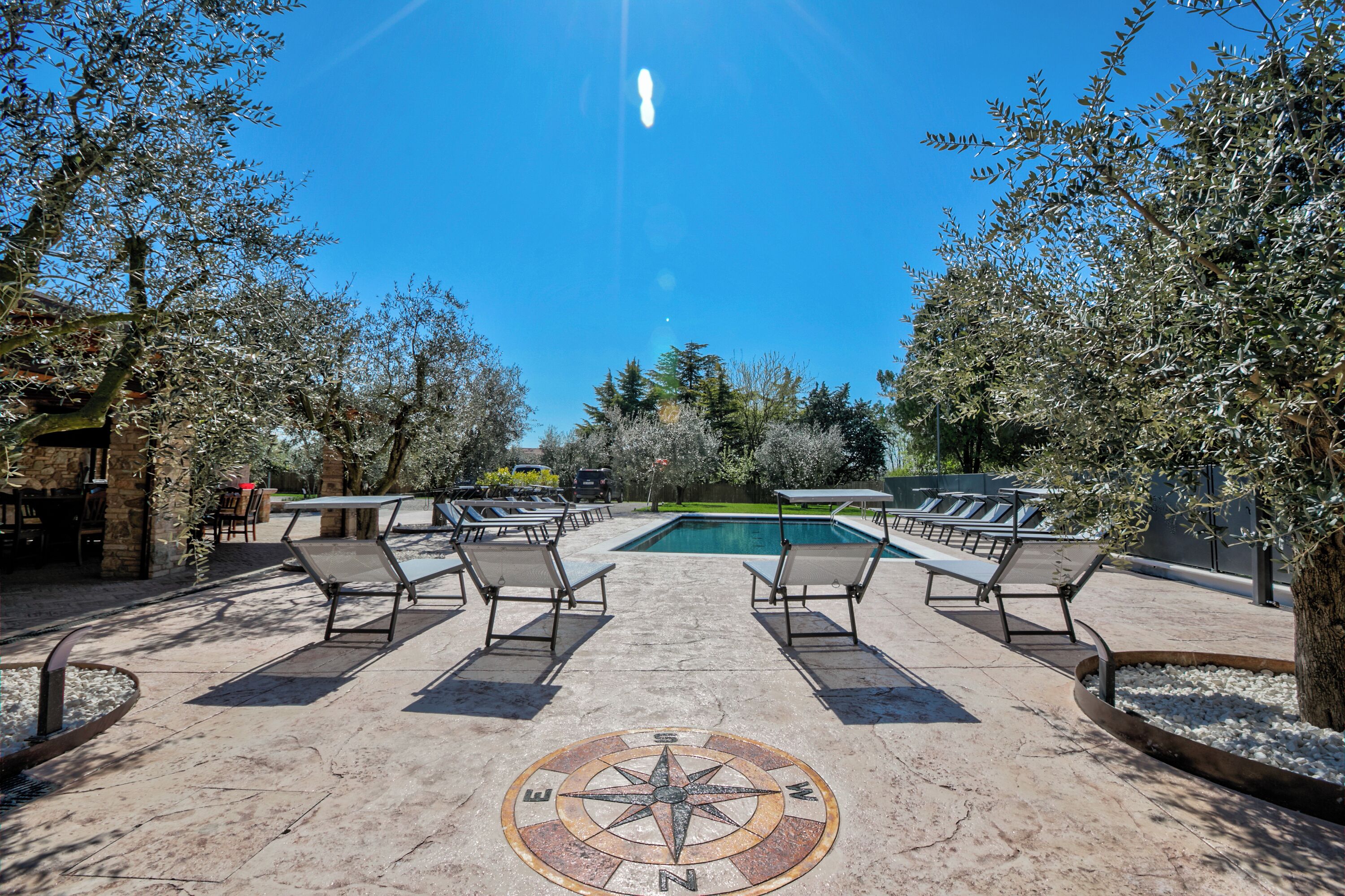 A pool area with lounge chairs, a compass design on the ground, and a clear blue sky.