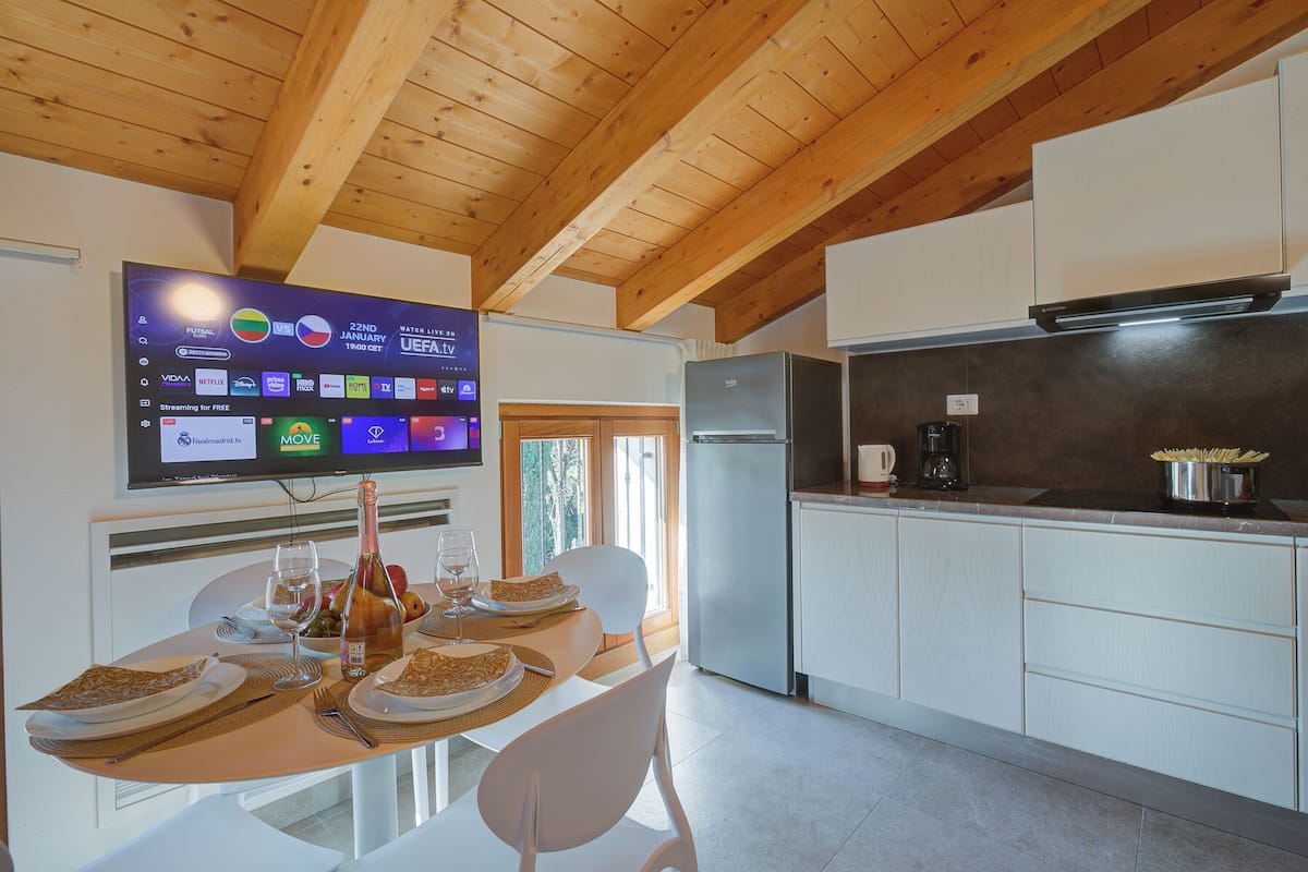 A modern kitchen with a built-in TV, dining table set for four, and a refrigerator.