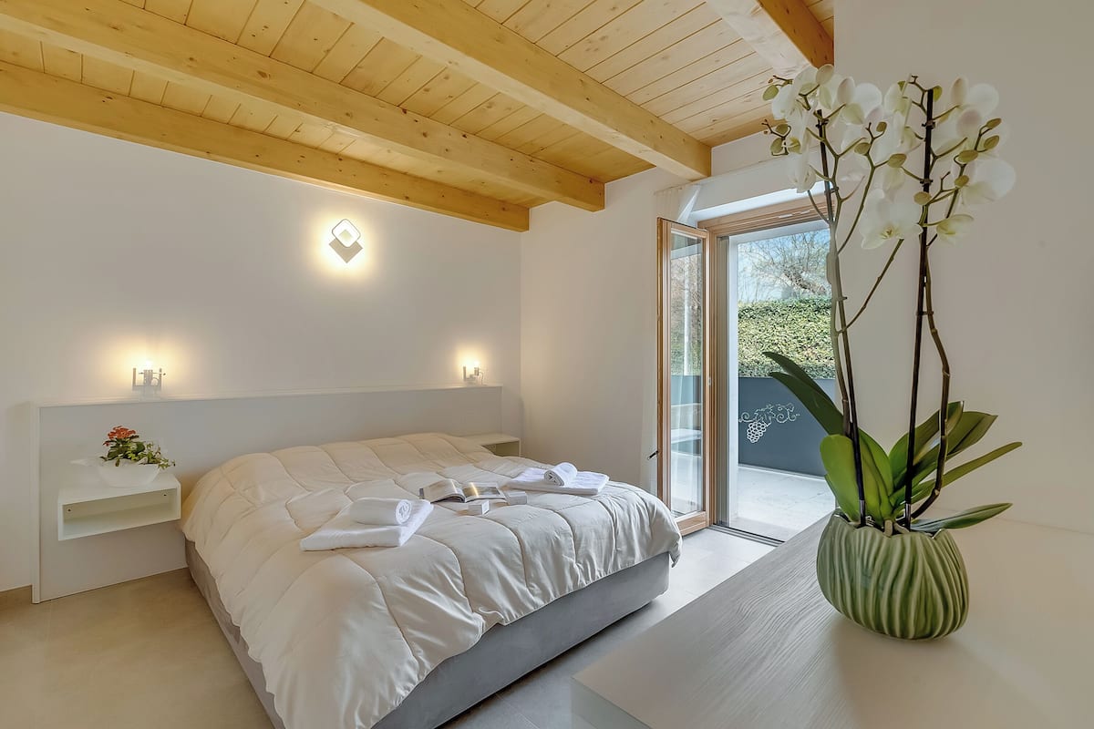 A bedroom with a bed, bedside tables, a potted orchid, and a view through a glass door.