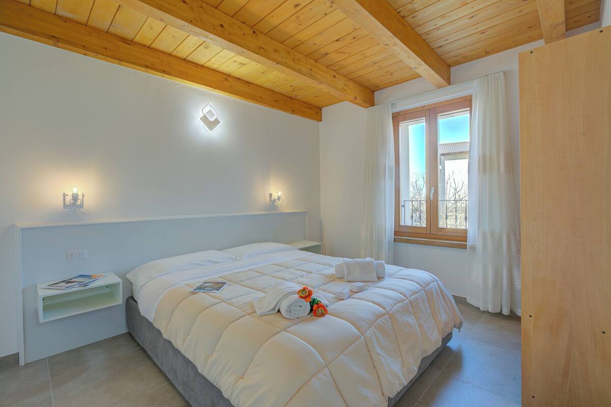 A bedroom with a bed, bedside tables, a window, and wooden ceiling beams.