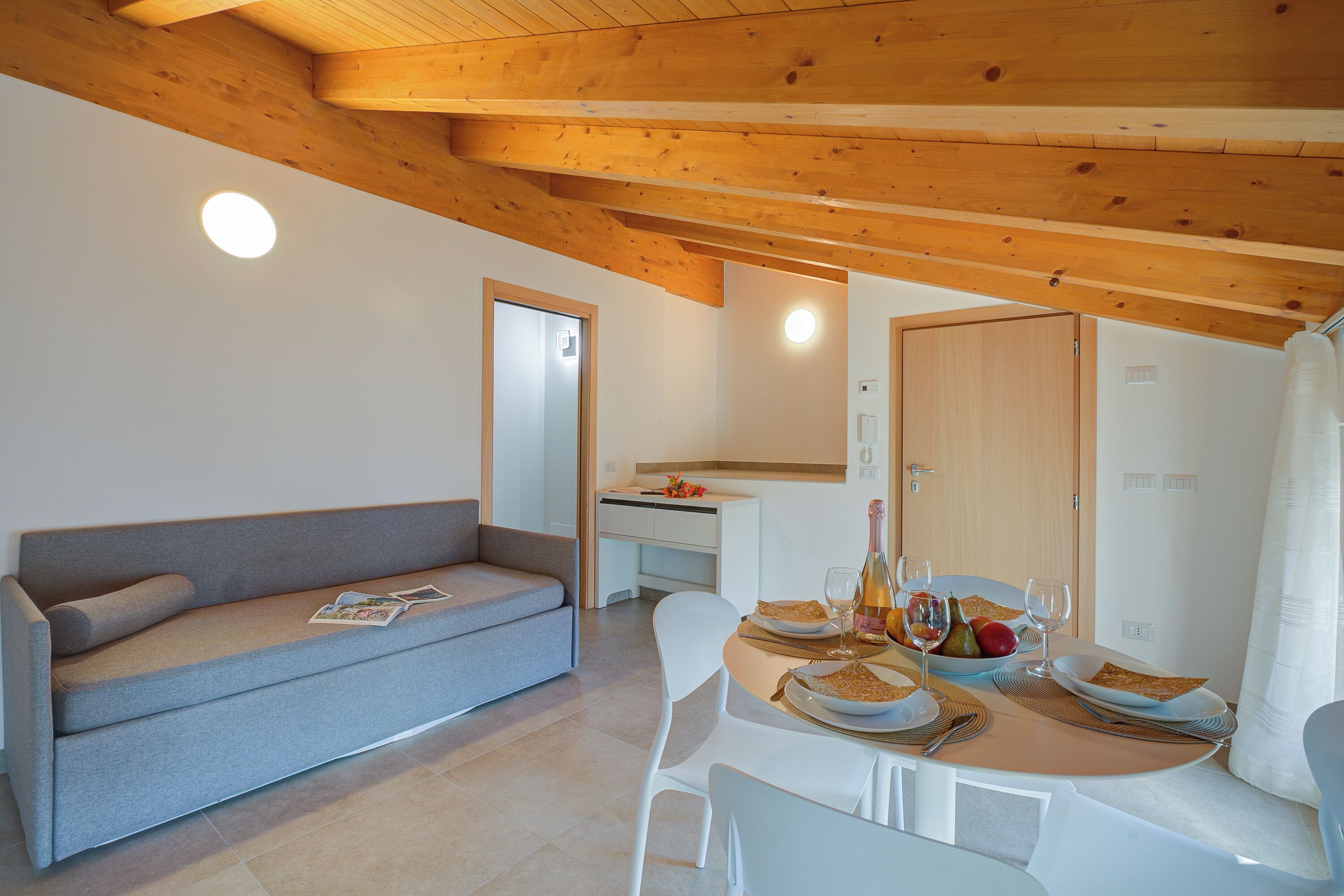 A modern interior with a sofa, dining table, and wooden ceiling beams.