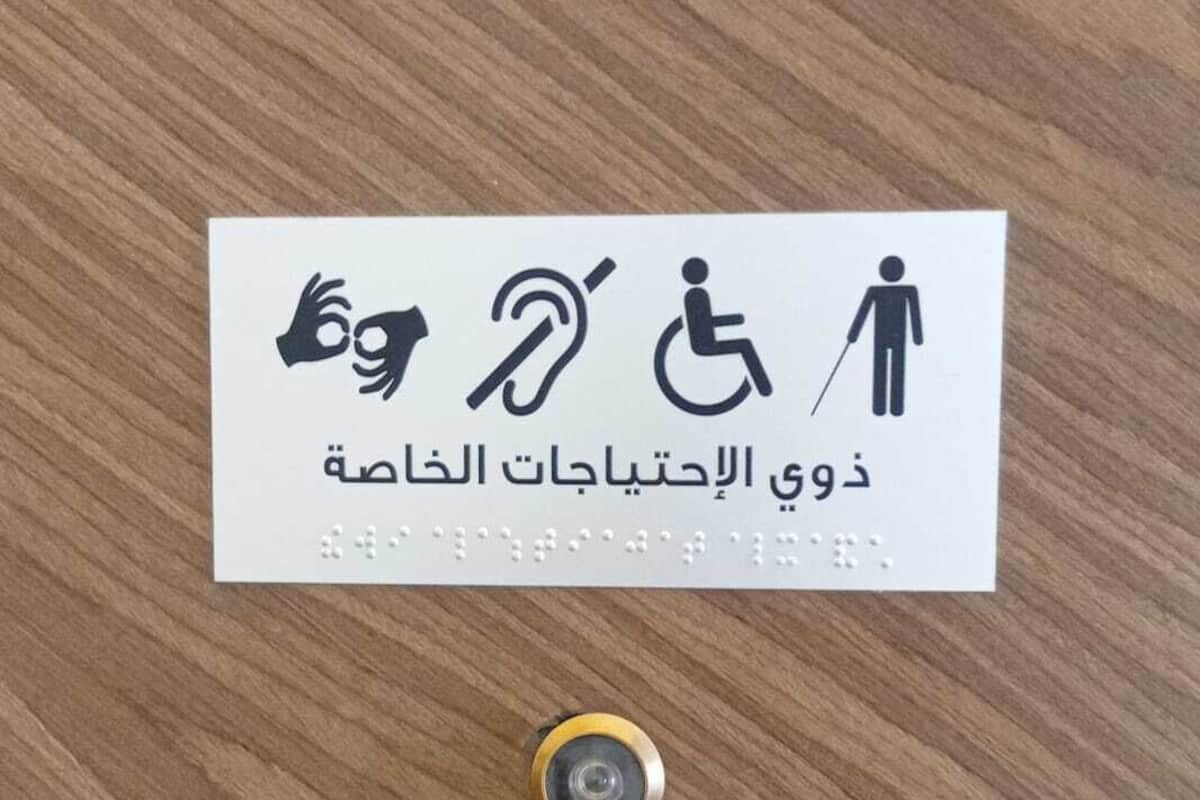 Un letrero con símbolos de accesibilidad y texto en árabe sobre una superficie de madera.