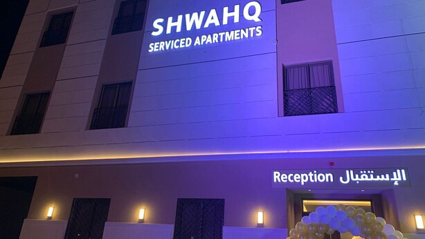 Ένα κτίριο με μια πινακίδα που αναγράφει «SHWAHQ Serviced Apartments» και μια περιοχή υποδοχής με μια πινακίδα στα αραβικά.