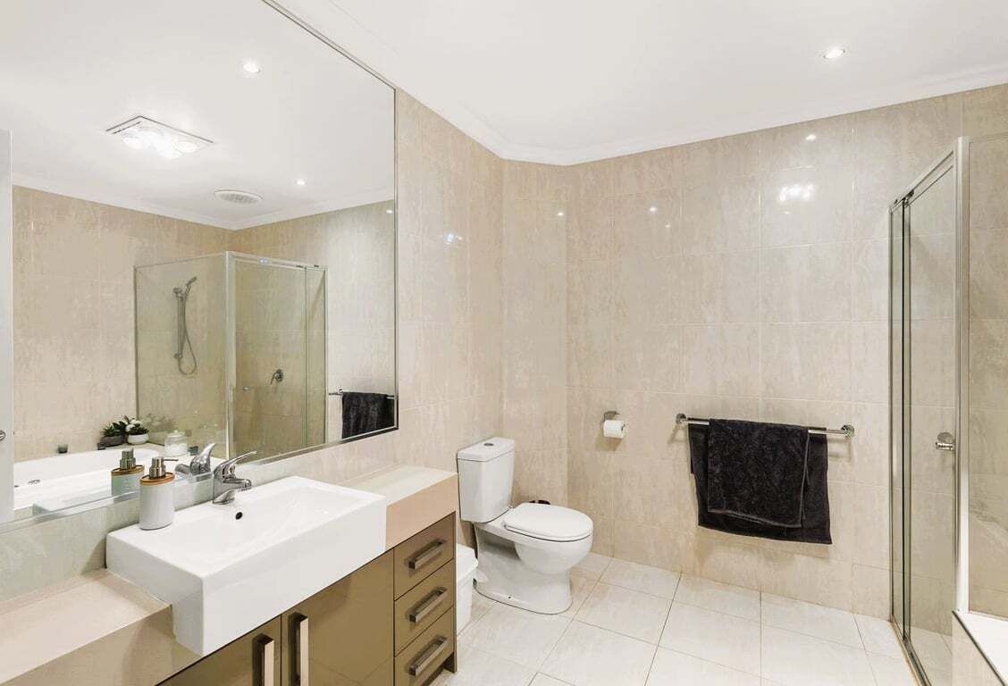 A modern bathroom with a large mirror, a shower enclosure, a toilet, and a sink.