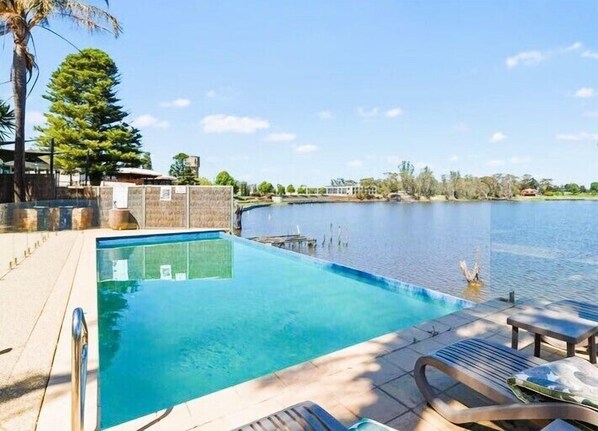 A swimming pool with a view of a body of water and a dock, surrounded by a deck with lounge chairs.