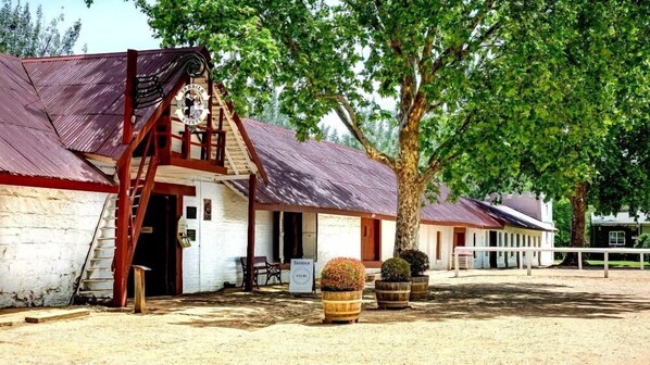 A rustic barn-style building with a wooden staircase leading to a door, surrounded by trees and a fenced area.