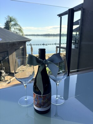 A bottle of Shiraz wine with a bow, two empty wine glasses, and a view of a body of water and buildings.