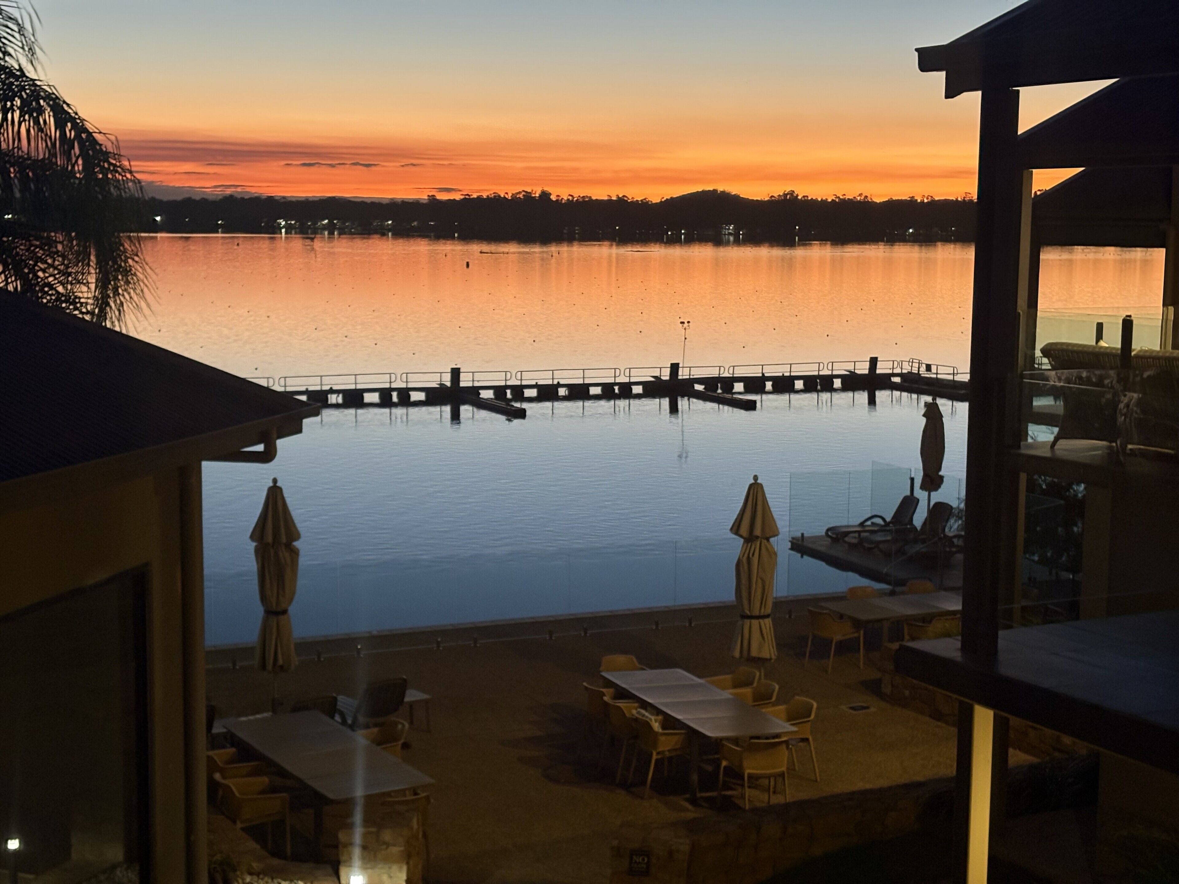A waterfront view with a dock, outdoor seating, and a calm lake at sunset.