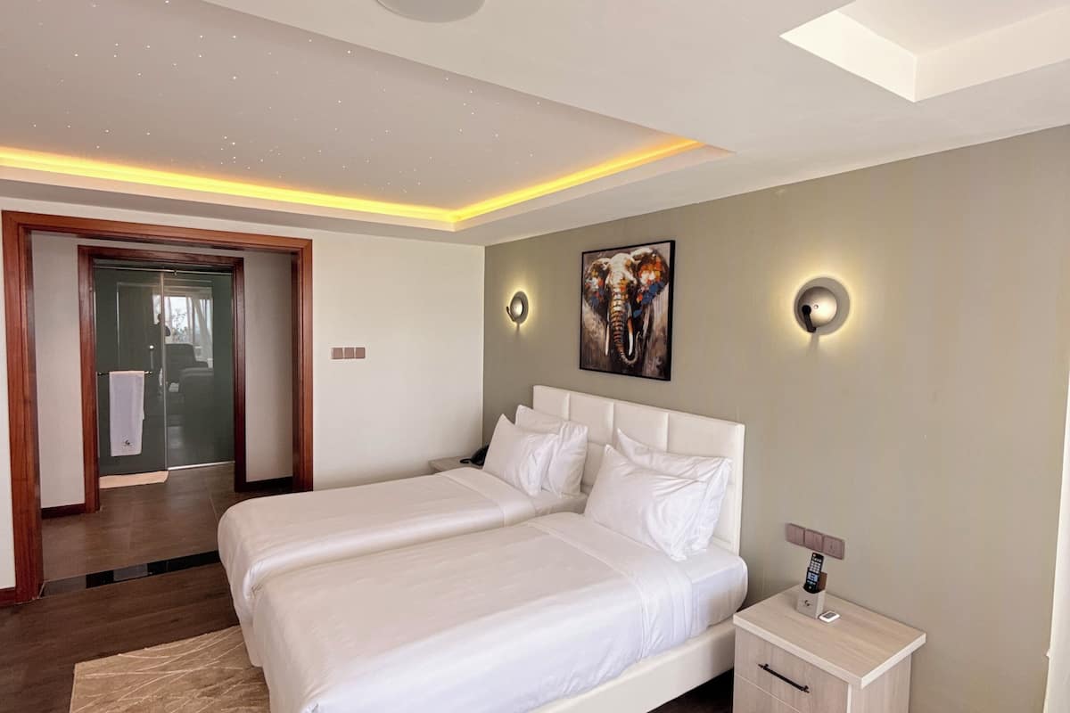 A modern bedroom with a large bed, bedside tables, a painting, and a ceiling light.