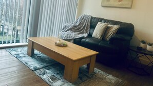 Ett vardagsrum med ett soffbord i trä, en svart lädersoffa och en tavla på väggen.
