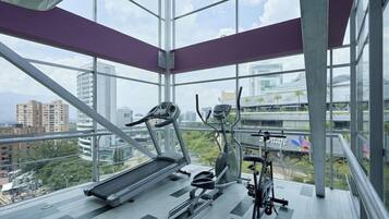 Un gimnasio con equipo de ejercicio y amplios ventanales con vistas a la ciudad.
