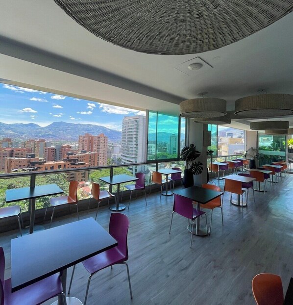 A modern dining area with large windows, a city view, and a variety of seating arrangements.