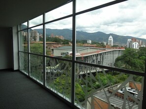 A room with large windows offering a view of a cityscape with buildings and mountains. - BH Poblado (Medellín)